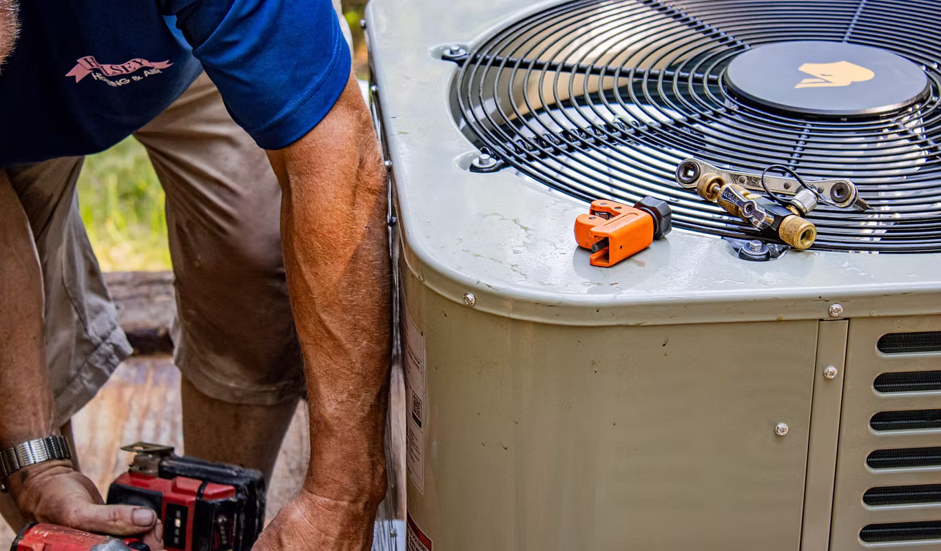 HVAC technician servicing an outdoor air conditioning condenser unit with maintenance tools during a residential AC inspection.